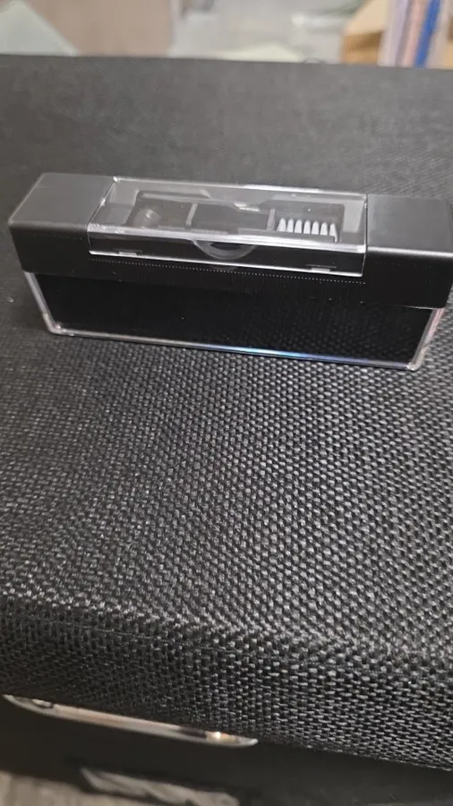 Velvet block with its clear sliding cover closed, standing on a black fabric speaker cabinet with records stacked behind it