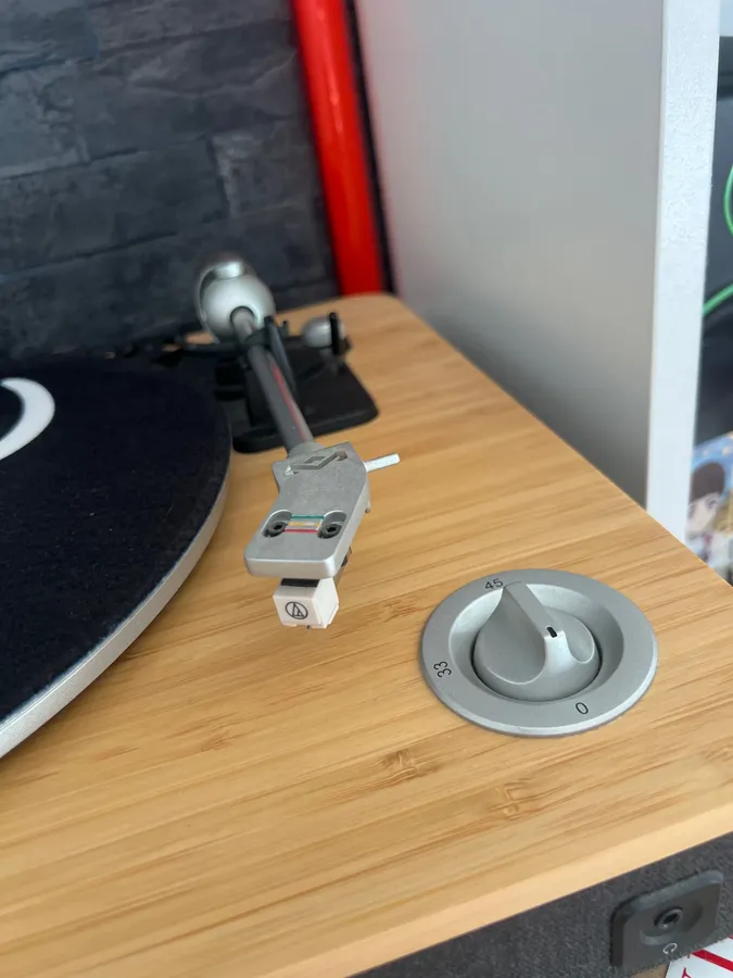 Close-up of a turntable tonearm and cartridge on a bamboo plinth, next to the 33 and 45 speed dial