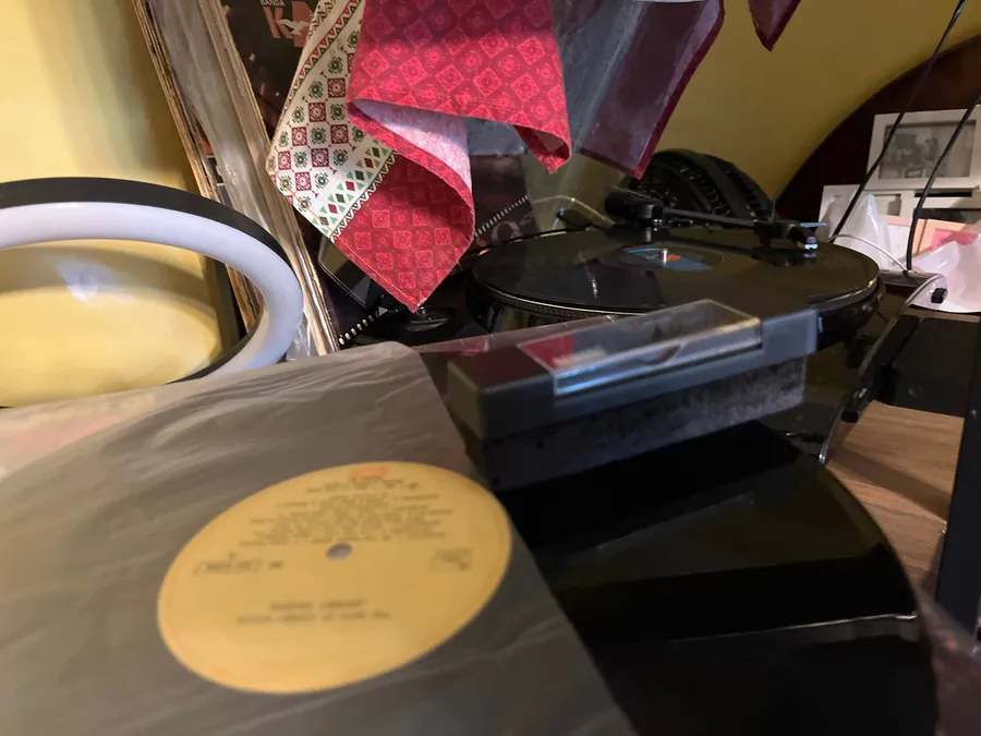 Record spinning on a turntable with the velvet block resting on the plinth and a sleeved LP in the foreground